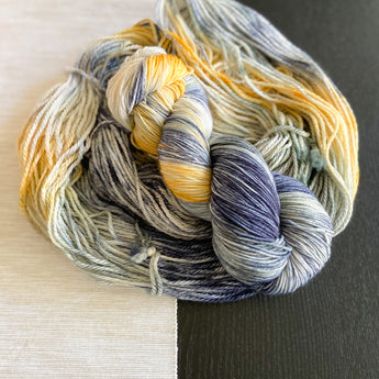 A skein of hand dyed yarn laid on top of more hand dyed yarn